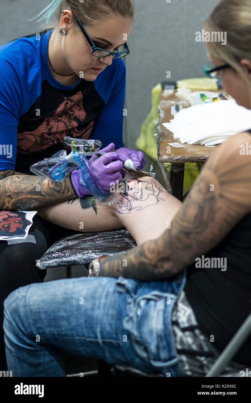 Tatuaggio. Tattooist femmina Claire Jackson tatuaggio un disegno sulla gamba di un cliente al Cornwall Tattoo Convention. Foto Stock