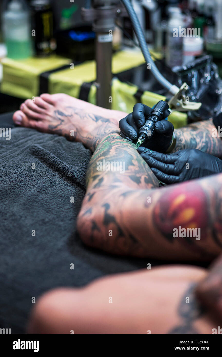 Tatuaggio. Un tattooist applicando un tatuaggio alla gamba di un cliente al Cornwall Tattoo Convention. Foto Stock