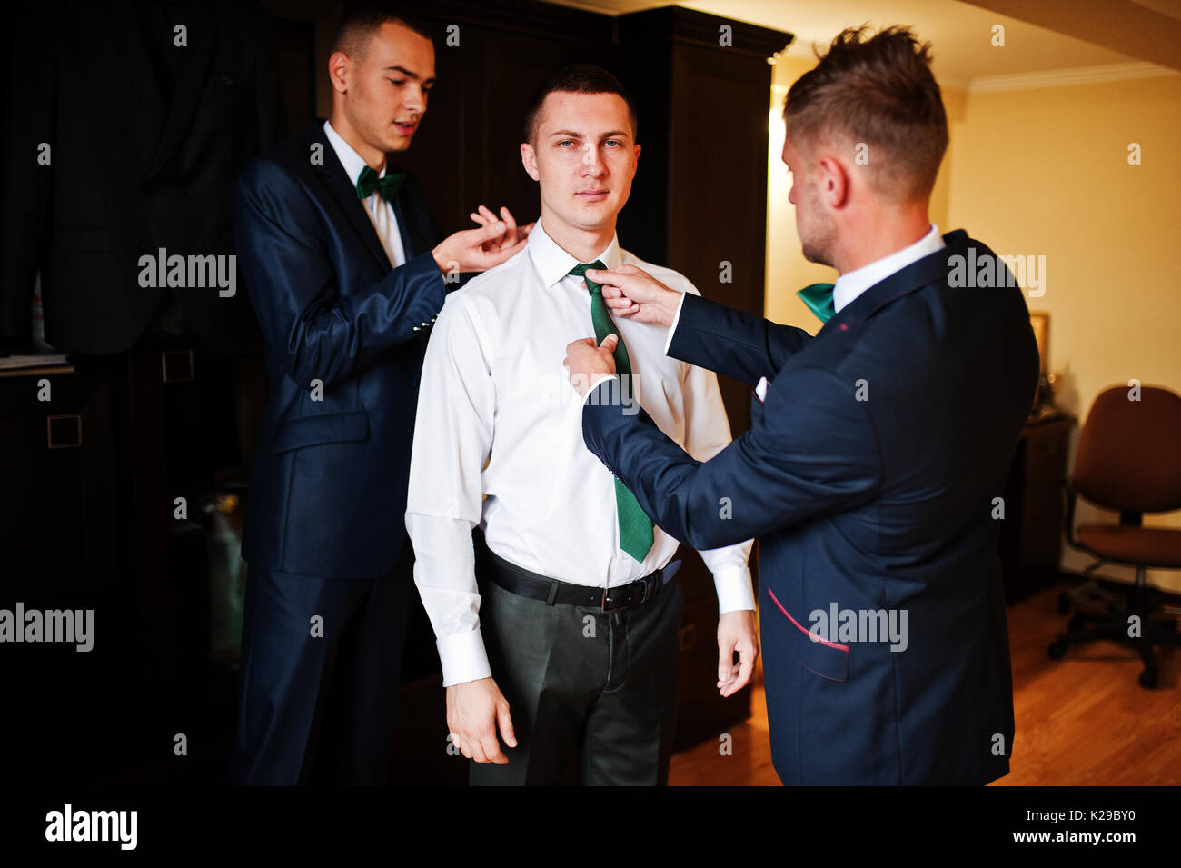 Groomsmen aiutare lo sposo a vestire e preparatevi per la sua cerimonia nuziale. Foto Stock