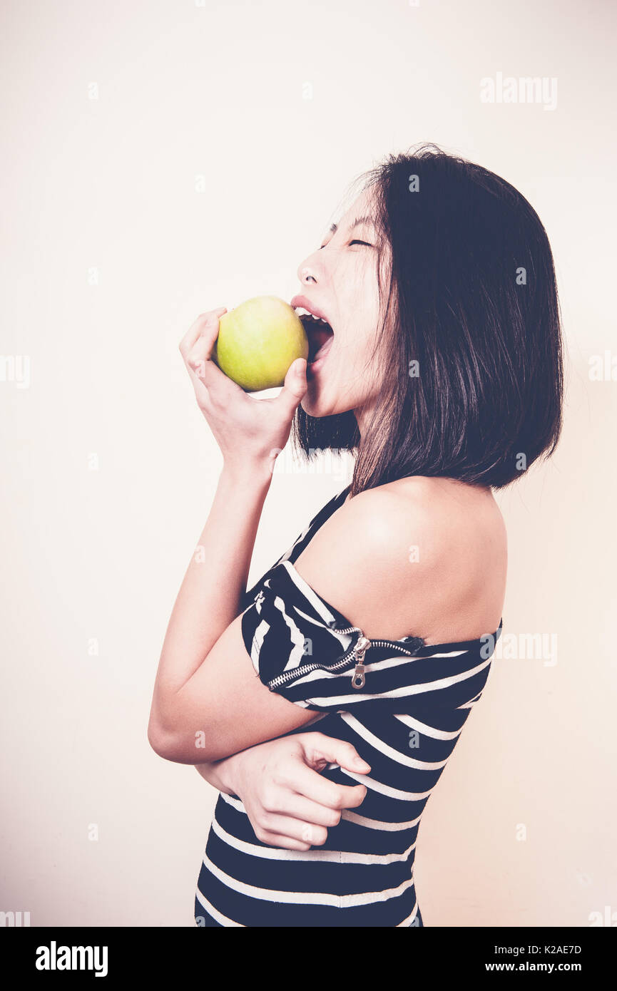 Giovane bella donna asiatica di mordere mela verde con espressione affamati, profilo su sfondo bianco Foto Stock