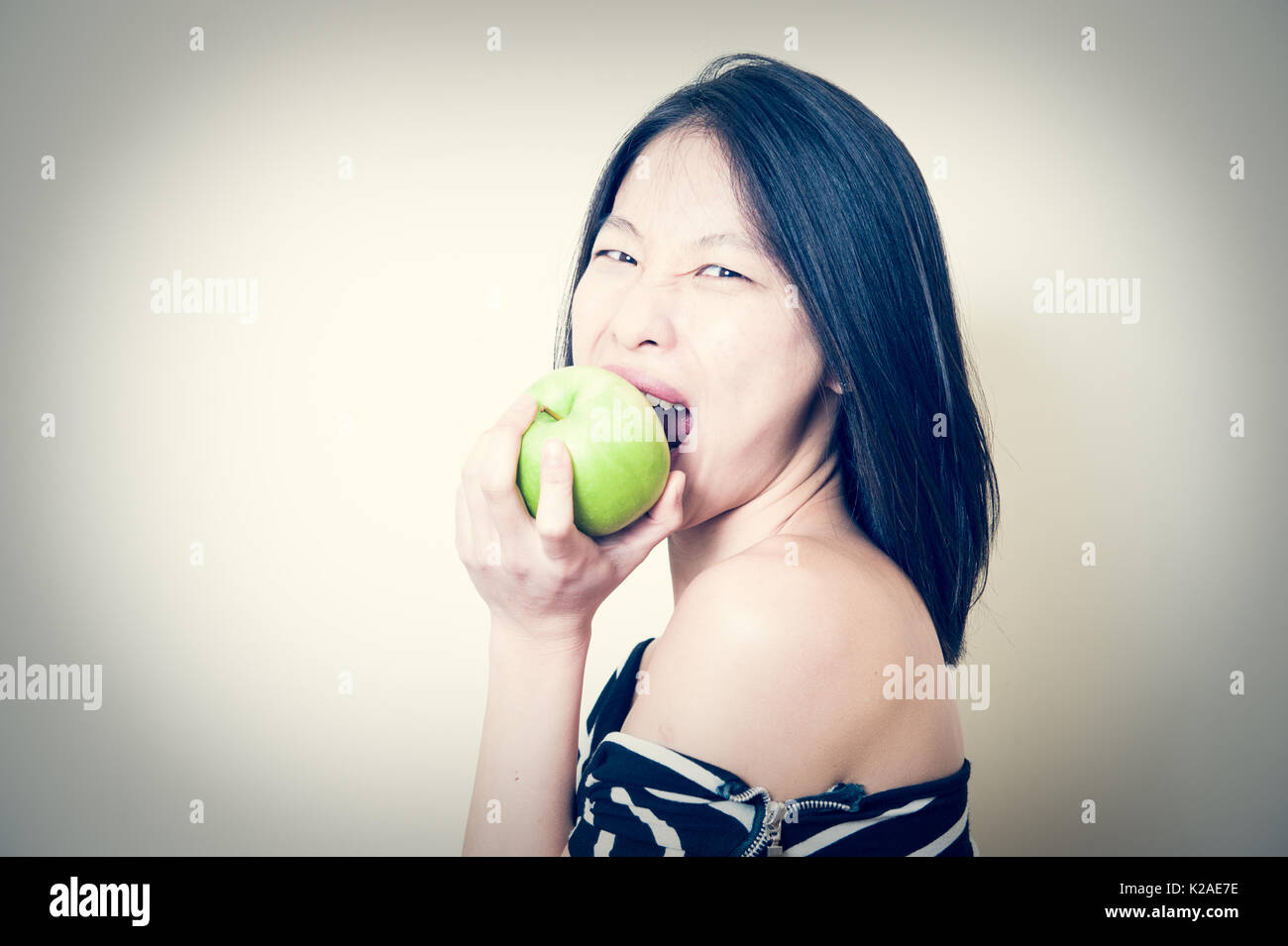 Giovane bella donna asiatica di mordere mela verde con espressione affamati, guardando la fotocamera ritratto su sfondo bianco Foto Stock