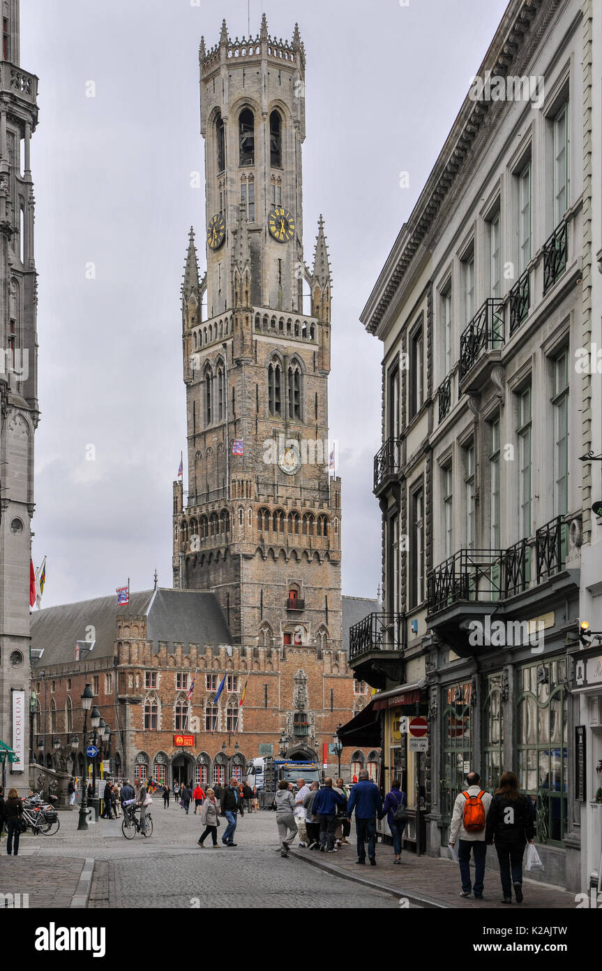 Turisti in giro per i negozi e la piazza del mercato, avvicinando il campanile medievale della città antica di brugge / bruges nelle Fiandre occidentali, Belgio Foto Stock