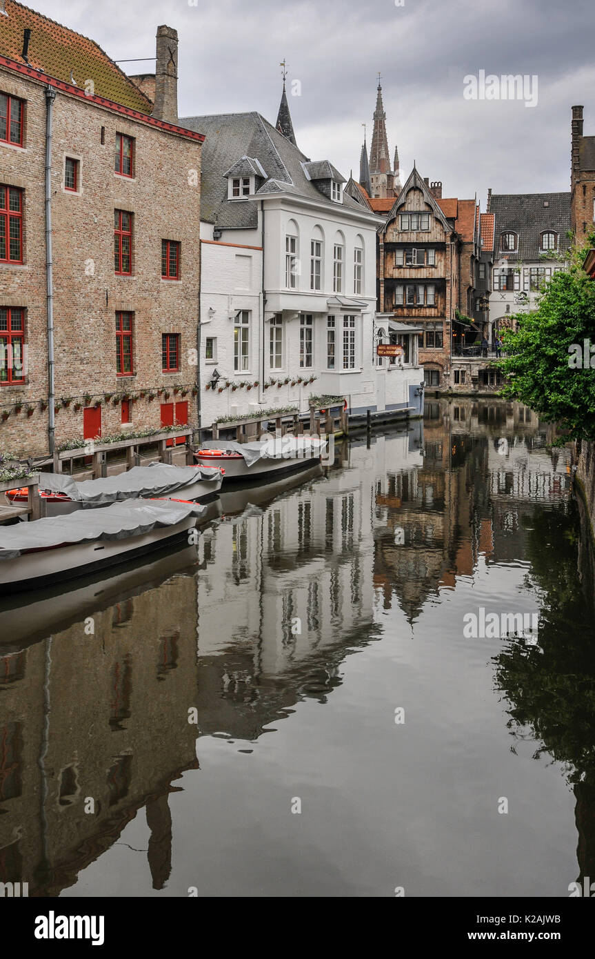 Edifici medievali della città antica di brugge / bruges riflessa in un tranquillo canale con le barche attraccate in Fiandra occidentale, Belgio Foto Stock