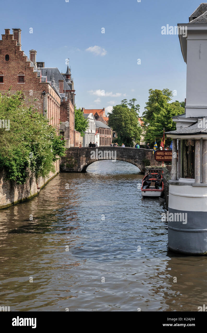 I turisti su un ponte su un tranquillo canale stretto con la barca ormeggiata nel medioevo West Flanders città di Brugge / Bruges in Belgio. Foto Stock