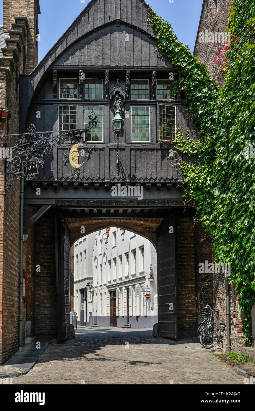 Il legno nero edificio rivestito su un arco nella città medievale di Brugge / Bruges in Belgio nell'estate al sole con un oro Half moon emblema Foto Stock