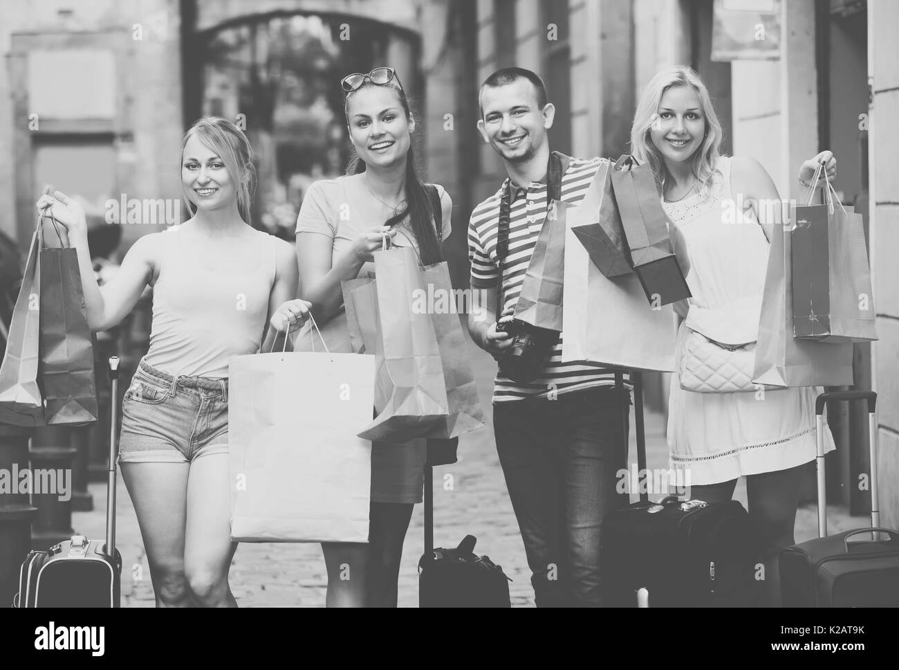 Quattro giovani gioiosi adulti guardando soddisfatto in piedi con la carta borse per lo shopping in città Foto Stock