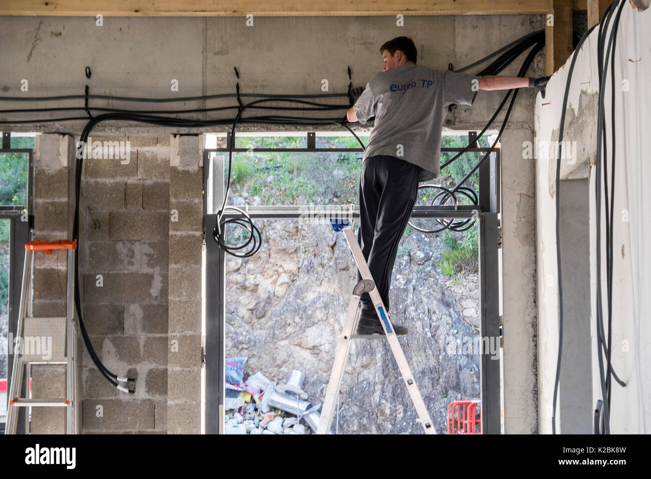 Elettricista su una scala opere per installare i cavi elettrici in una nuova casa in costruzione nel sud della Francia Foto Stock