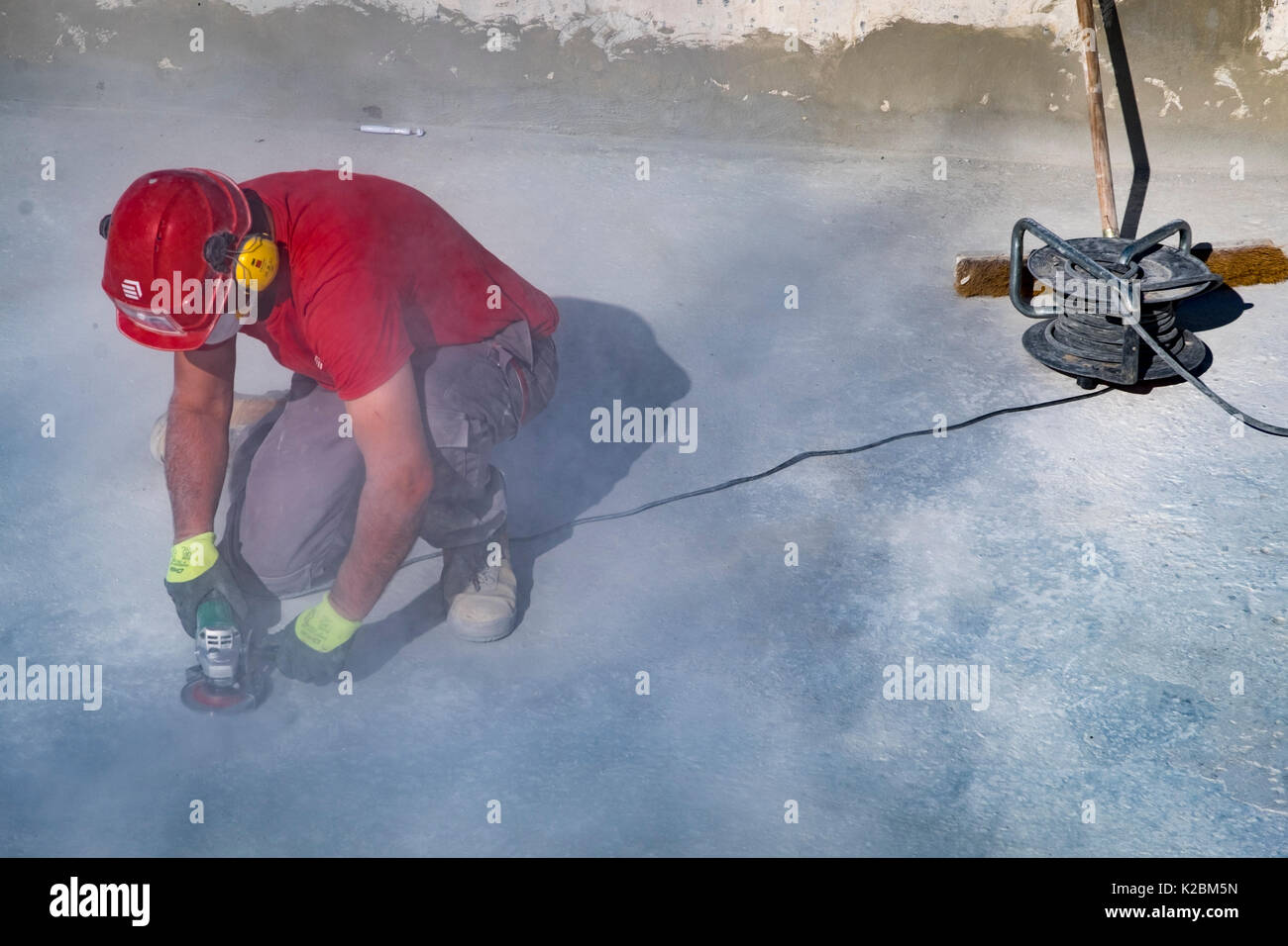 Costruzione Lavoratore che indossa il casco di sicurezza e le cuffie utilizza una macchina levigatrice per levigare il pavimento di una piscina Foto Stock