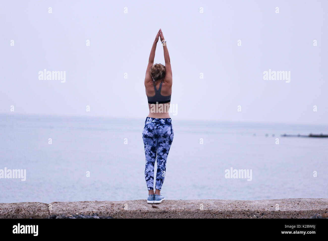 Giovane donna fare yoga sulla parete del mare a Cromer, Norfolk, Regno Unito. Foto Stock