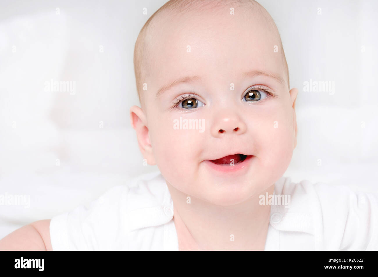 Sorridenti bambino con ampia aprire gli occhi marrone su sfondo bianco. close up verticale Foto Stock