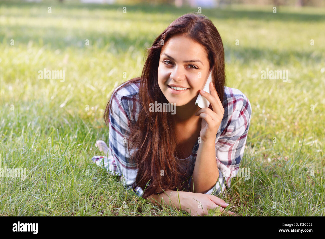 Bella ragazza adolescente giacente sul campo di erba verde e parlare per telefono. all'esterno. carina ragazza adolescente relax nel parco Foto Stock