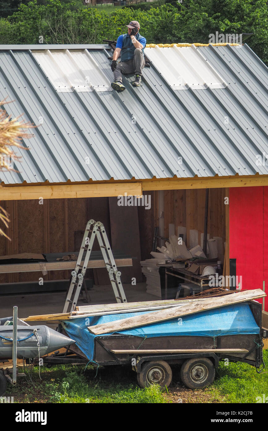 Un costruttore di copritetti sul tetto in acciaio costruzione lavoro in altezza senza tener conto delle procedure di sicurezza con cattive prassi in materia di sicurezza Foto Stock