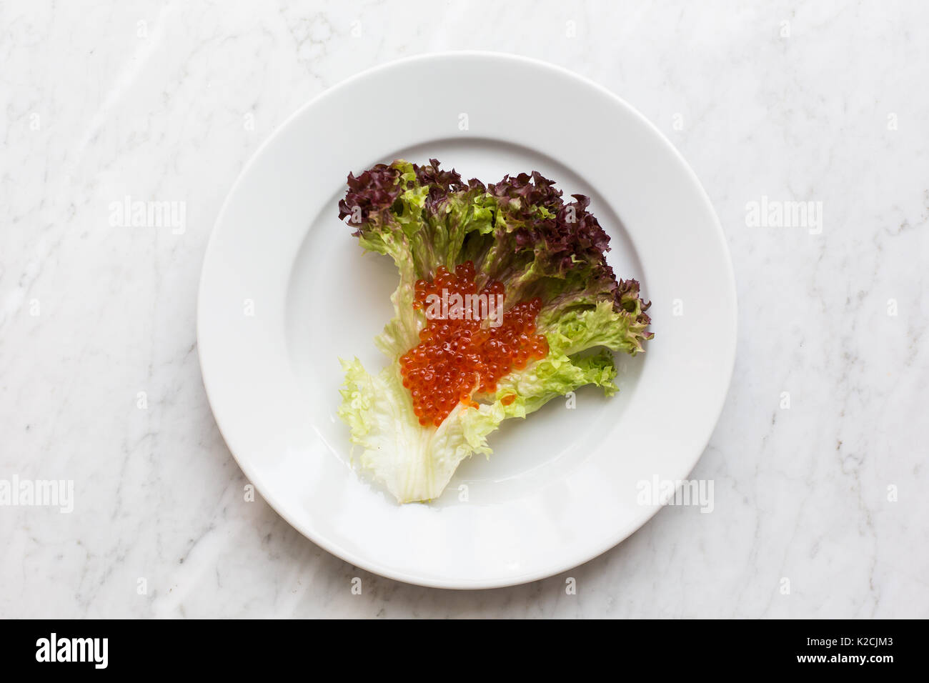 Vista superiore del caviale rosso su una foglia di insalata su una luce Sfondo marmo. copia spazio, vista dall'alto Foto Stock