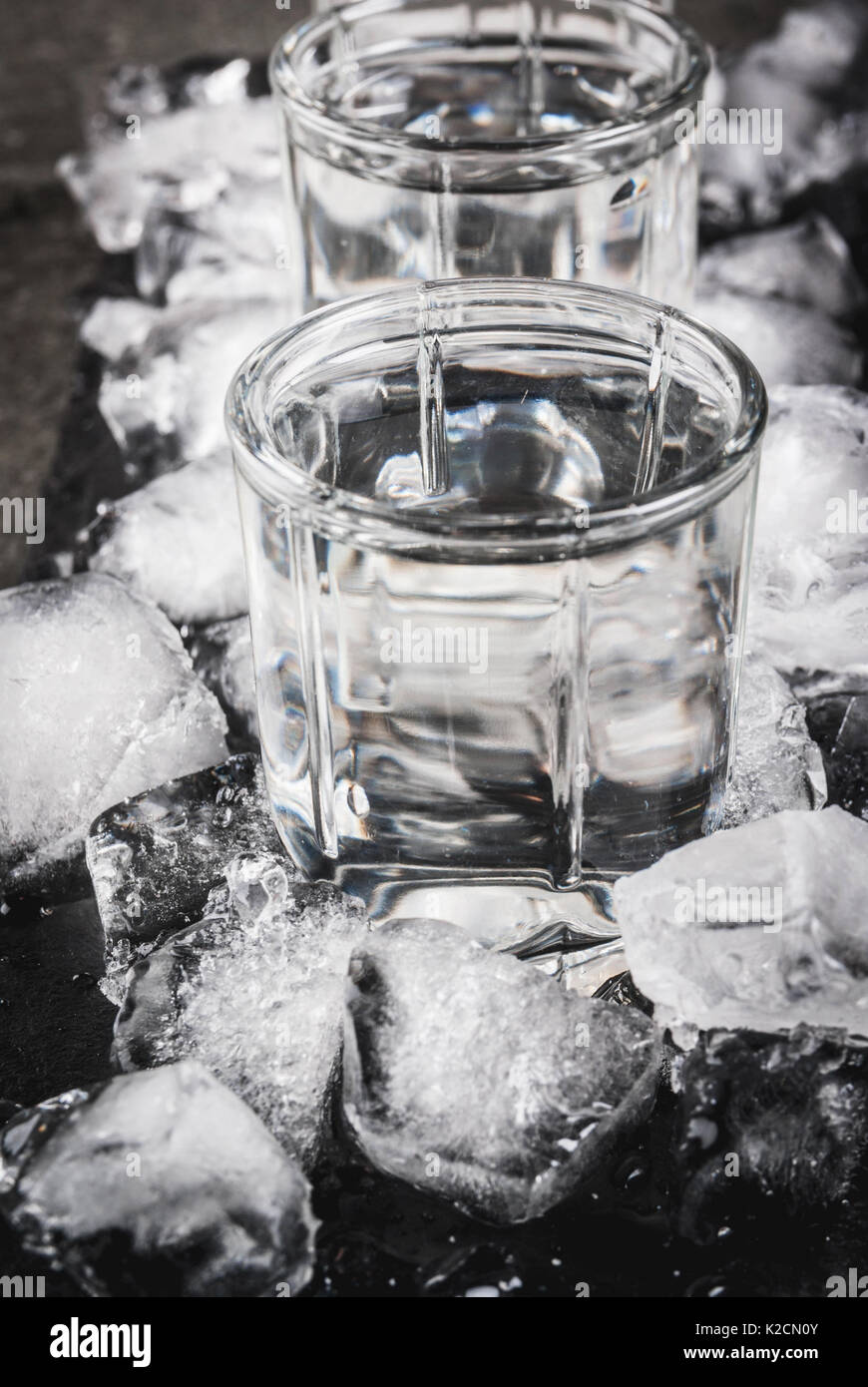 Alcol e cocktail. Tre Bicchieri di vodka su un vassoio di ardesia, con ghiaccio. Su una pietra nera tabella, Foto Stock