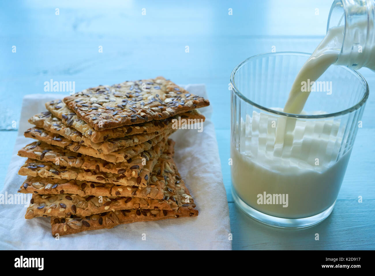 I cookie costituito da pasta sfoglia ricoperta con sesamo, chia e semi di girasole con latte versando dal flacone di vetro. angolo basso Foto Stock