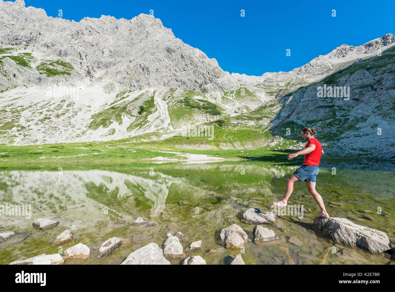 Escursionista saltando su una pietra, lago di montagna alla Printz Luitpolt House, Algovia Alpi, Bad Hindelang, Algovia, Baviera, Germania Foto Stock
