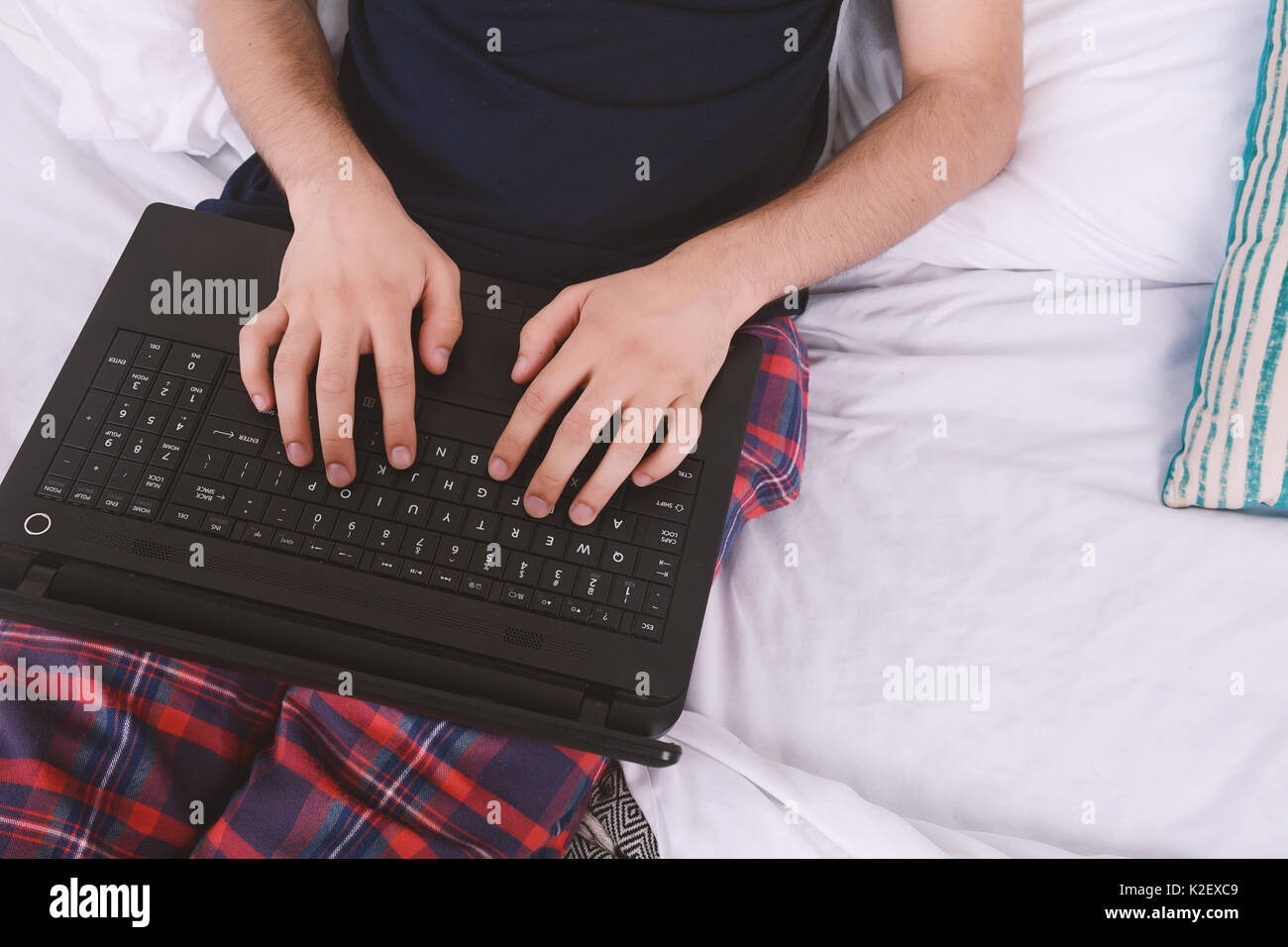 Attraente giovane uomo usando il suo computer portatile nel letto. In ambienti chiusi. Foto Stock