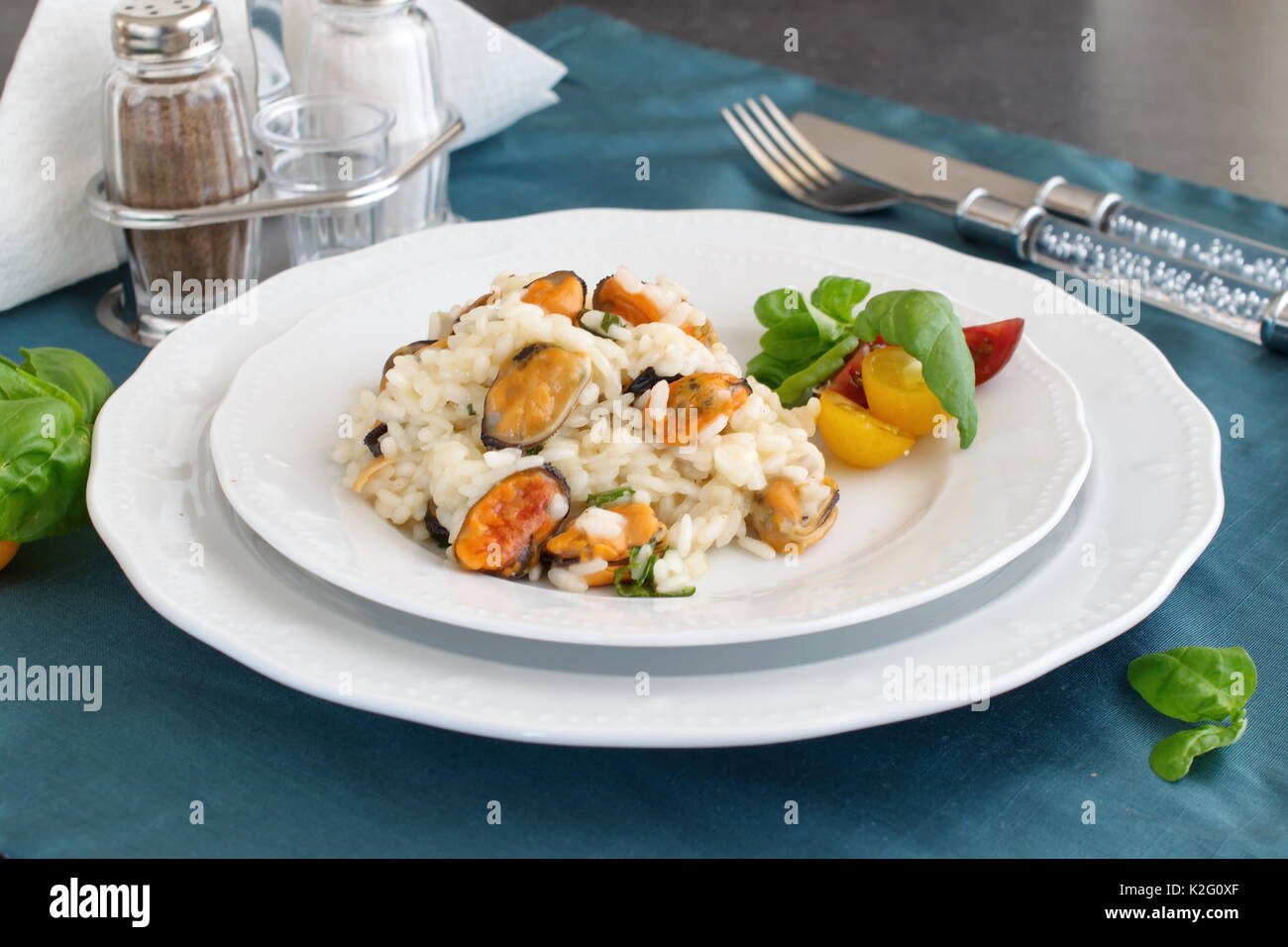 Risotto con le cozze su una piastra bianca con basilico, pomodori ciliegia su un panno verde. Mangiare sano concetto, Meditarranian stile di vita Foto Stock