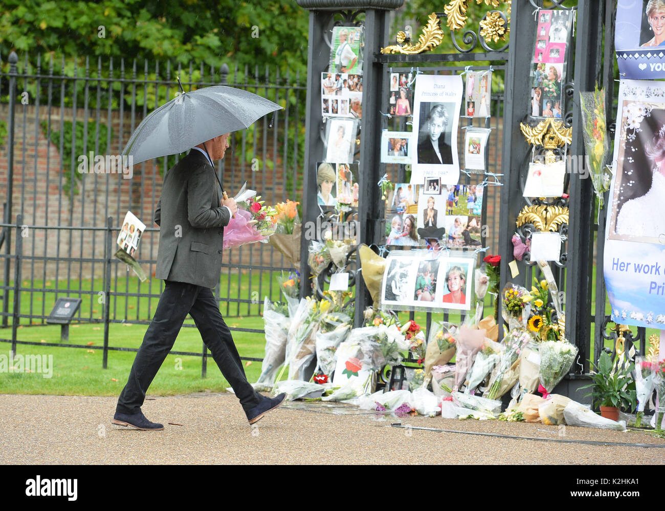 Il principe Harry prende un mazzo di fiori da un wellwisher per aggiungere ai tributi a Diana, principessa di Galles attaccato al Golden Gate di Kensington Palace di Londra, precedendo il ventesimo anniversario della la morte di sua madre. Foto Stock