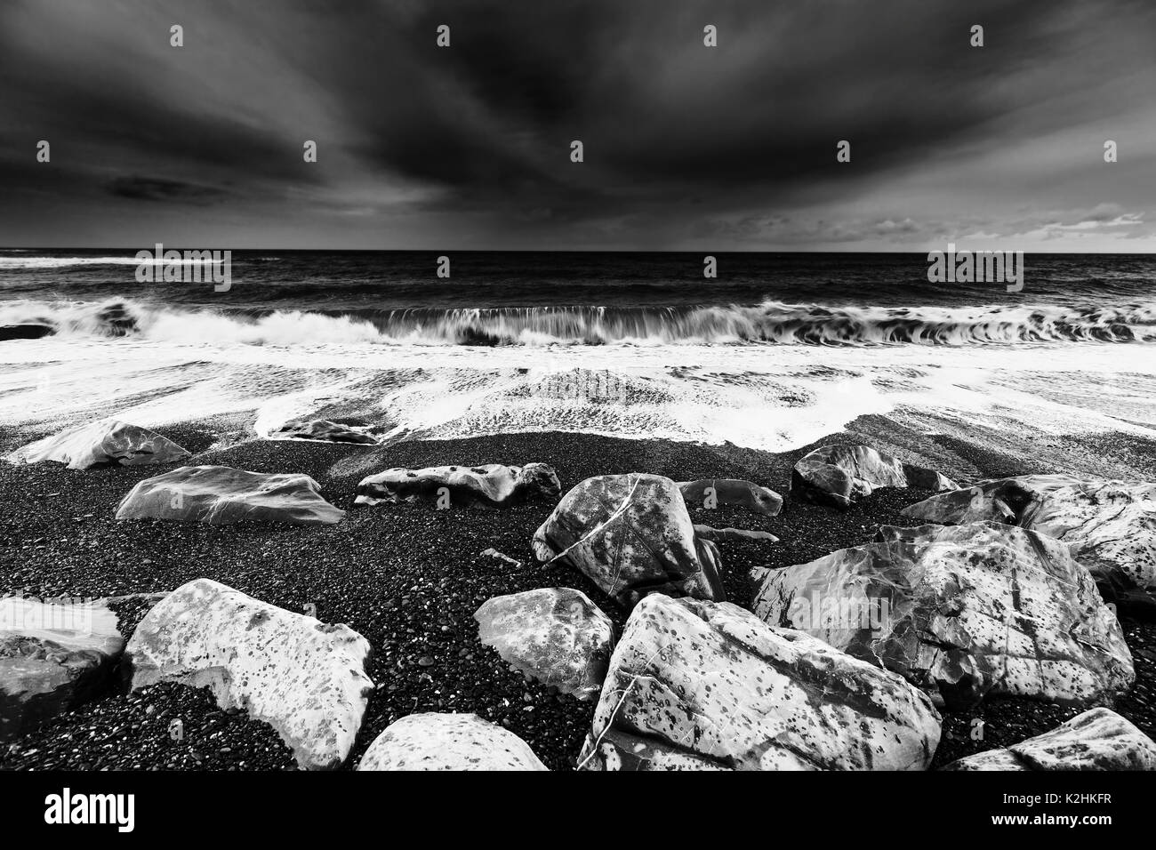 Ocean onde che si infrangono sulla spiaggia rocciosa, drammatica Seascape nel Galles del Nord, in bianco e nero Foto Stock