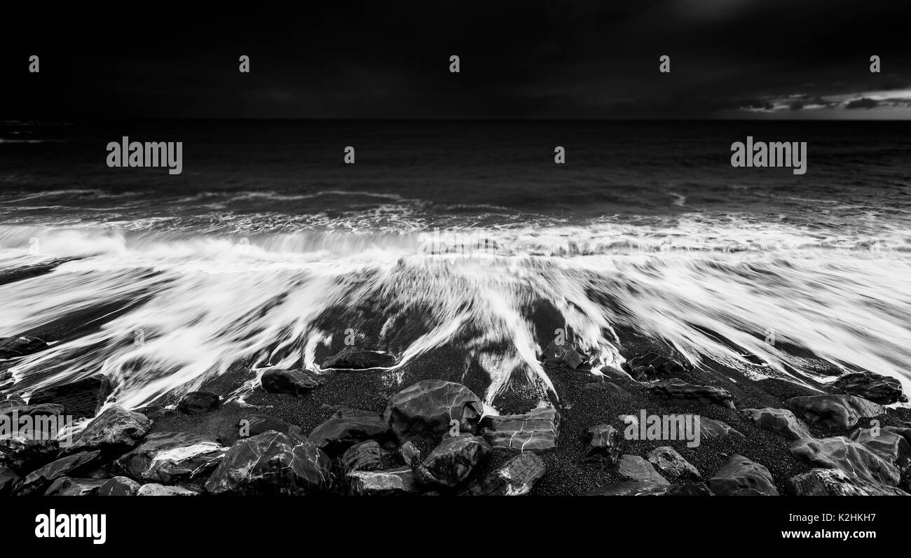 Oceano drammatico onde che si infrangono sulla spiaggia rocciosa, in bianco e nero Foto Stock