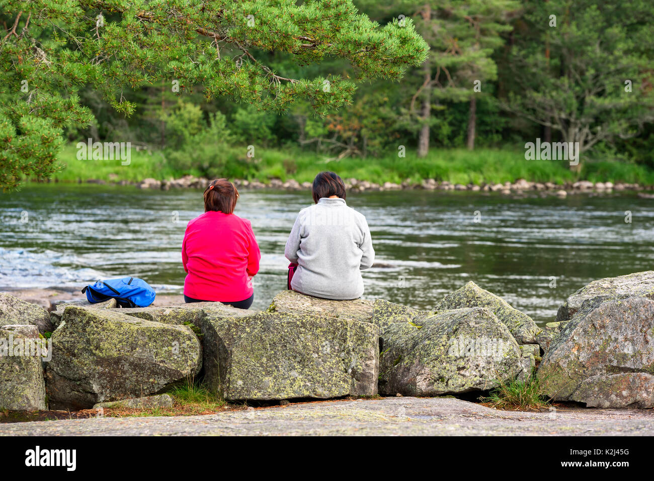 Setesdal, Norvegia - Agosto 16, 2017: documentario di viaggio di due donne seduti sulle pietre di fiume avente un talk, retrocede verso la telecamera. Fiume e f Foto Stock