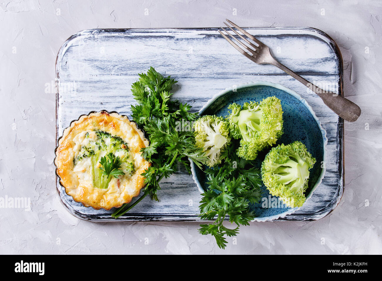 Cotto in casa verdure broccoli quiche torta in mini metallo forma servita con verdure fresche, piastra forcella su bianco che serve di bordo su cemento grigio backgro Foto Stock