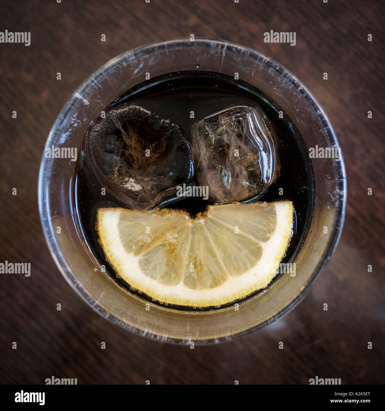 I cubetti di ghiaccio e una fettina di limone seduto in un bicchiere di coca cola formando una faccia sorridente Foto Stock