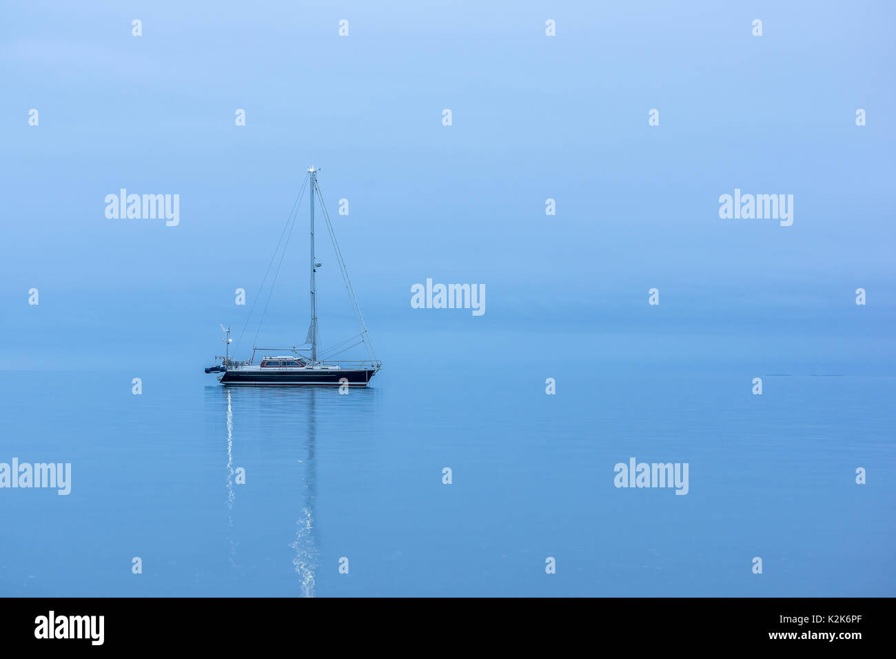 Nero solitario barca a vela in oceano prima dell'alba, riflessioni in blu ora Foto Stock
