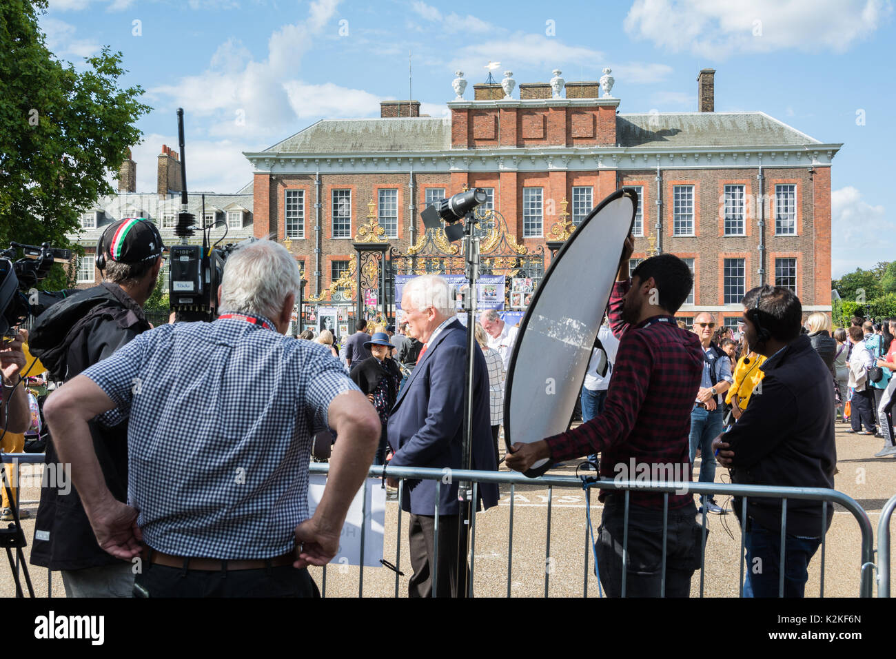 Un news reporter e cameraman con un pezzo alla telecamera fuori dalle porte di Kensington Palace. Per commemorare la Principessa Diana, venti anni dopo la sua morte. Foto Stock