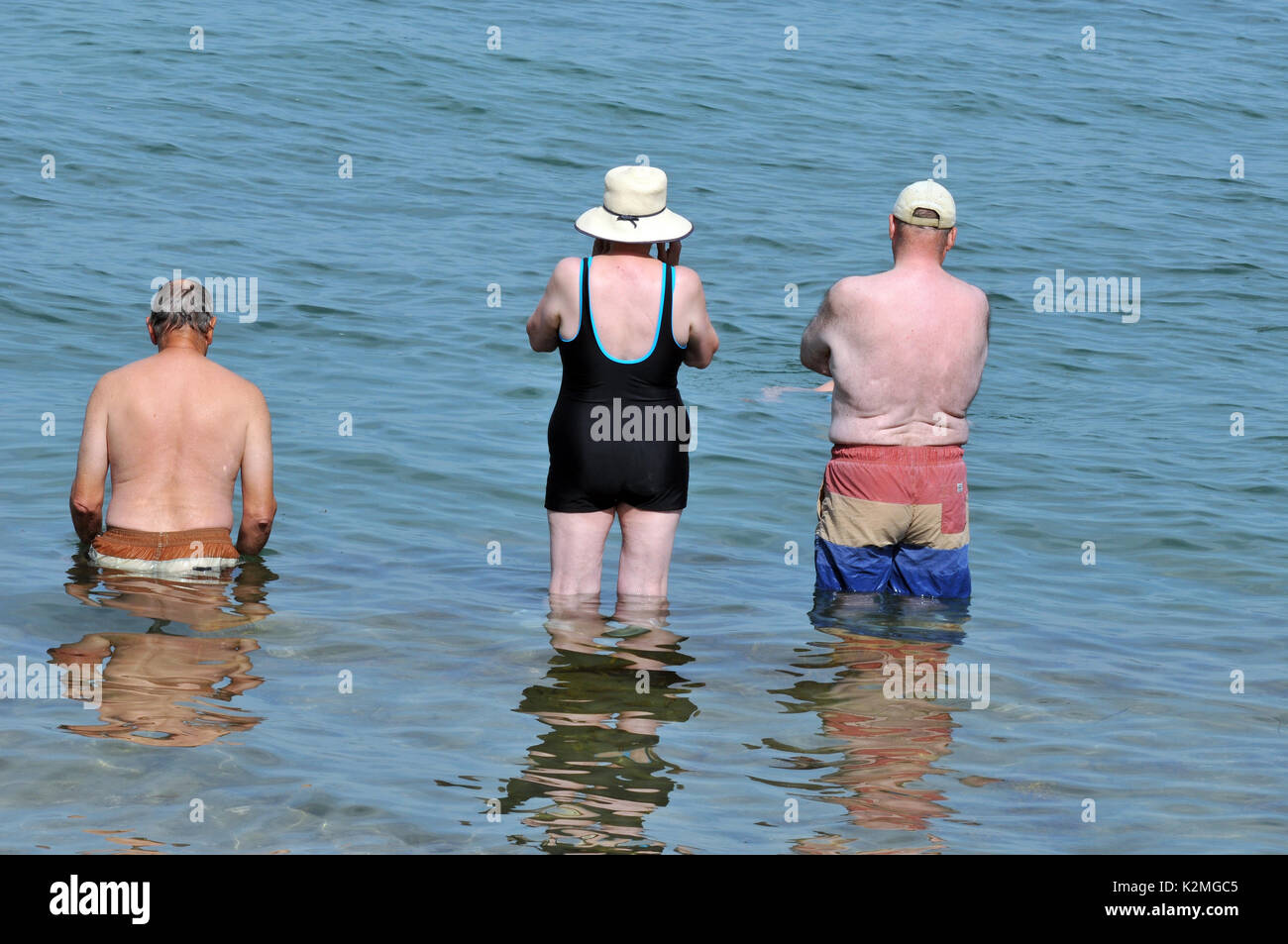 Tre anziani o persone in pensione due uomini una donna in piedi nel mare andando a nuoto con la schiena per la telecamera il pensionamento in pensione salute attività Foto Stock