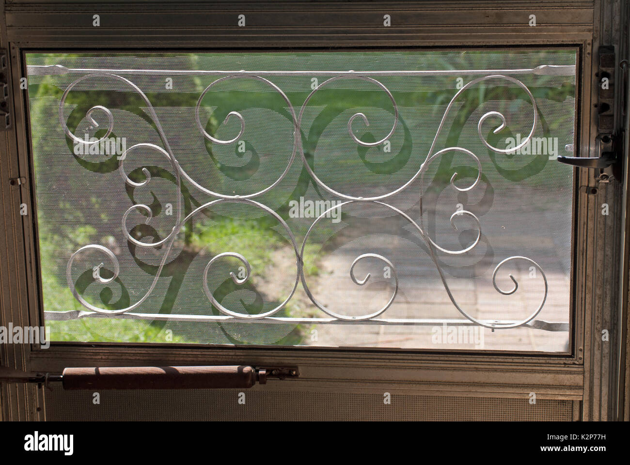 A metà secolo decorativi della griglia dello schermo su una finestra in una porta con erba e un patio dietro di essa Foto Stock