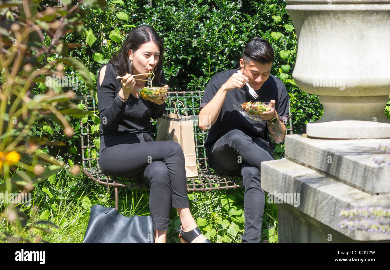 Coppia asiatica in Elizabeth Street Garden di Nolita in Lower Manhattan godendo takeaway insalate e sole Foto Stock