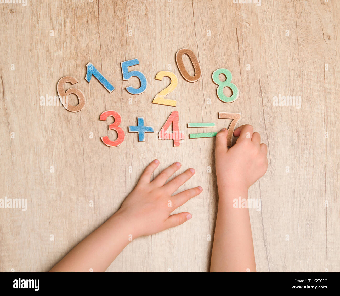 Le mani del bambino con una semplice equazione matematica contro il tavolo di legno Foto Stock