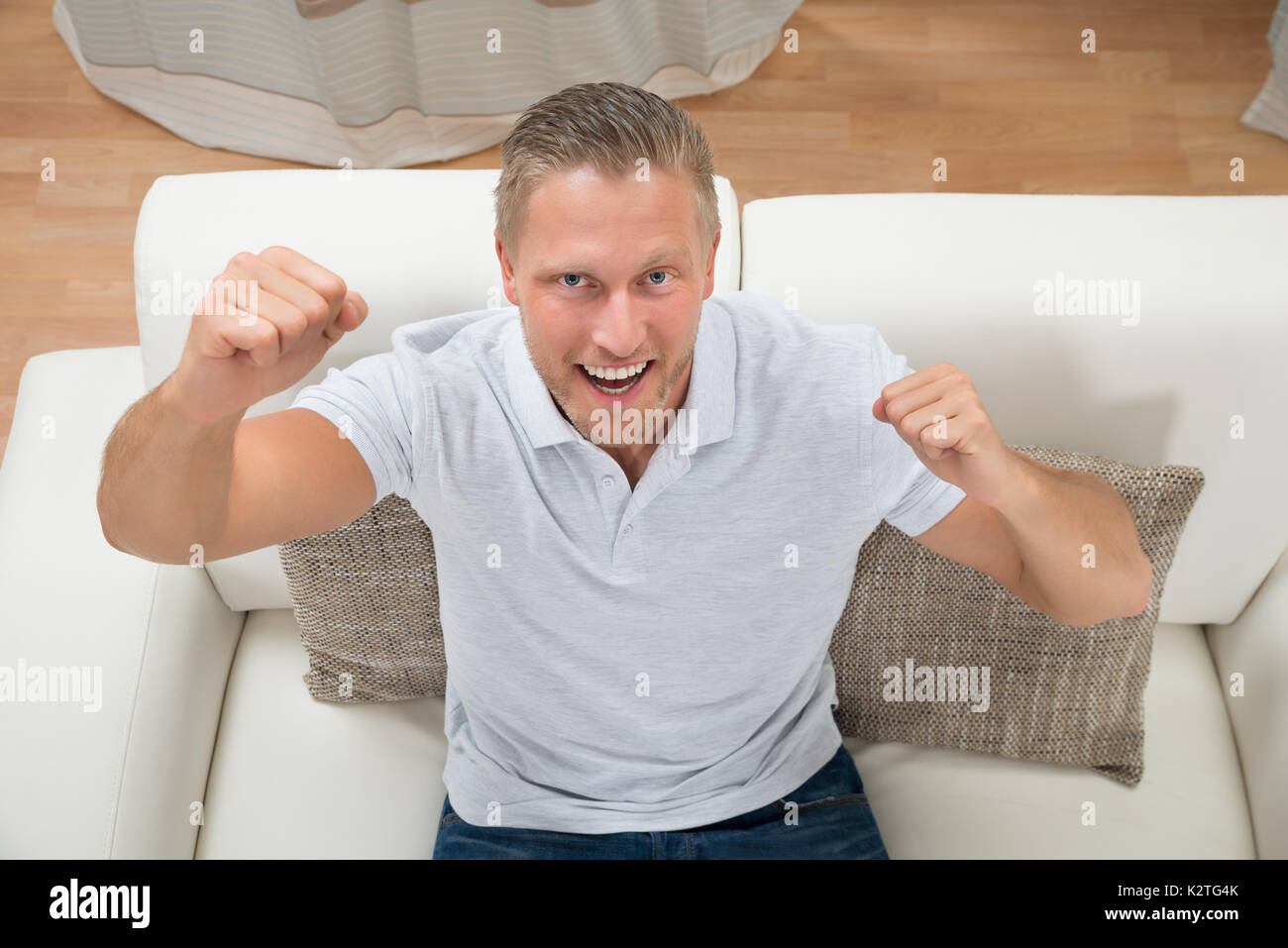 Ritratto di giovane uomo eccitato Clenching pugno sul divano Foto Stock