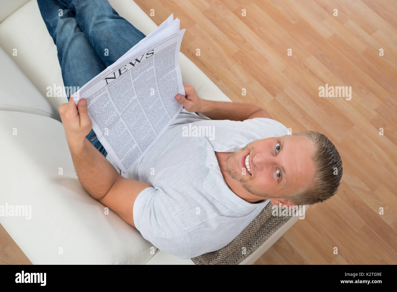 Giovane uomo felice sul divano bianco con quotidiano Foto Stock