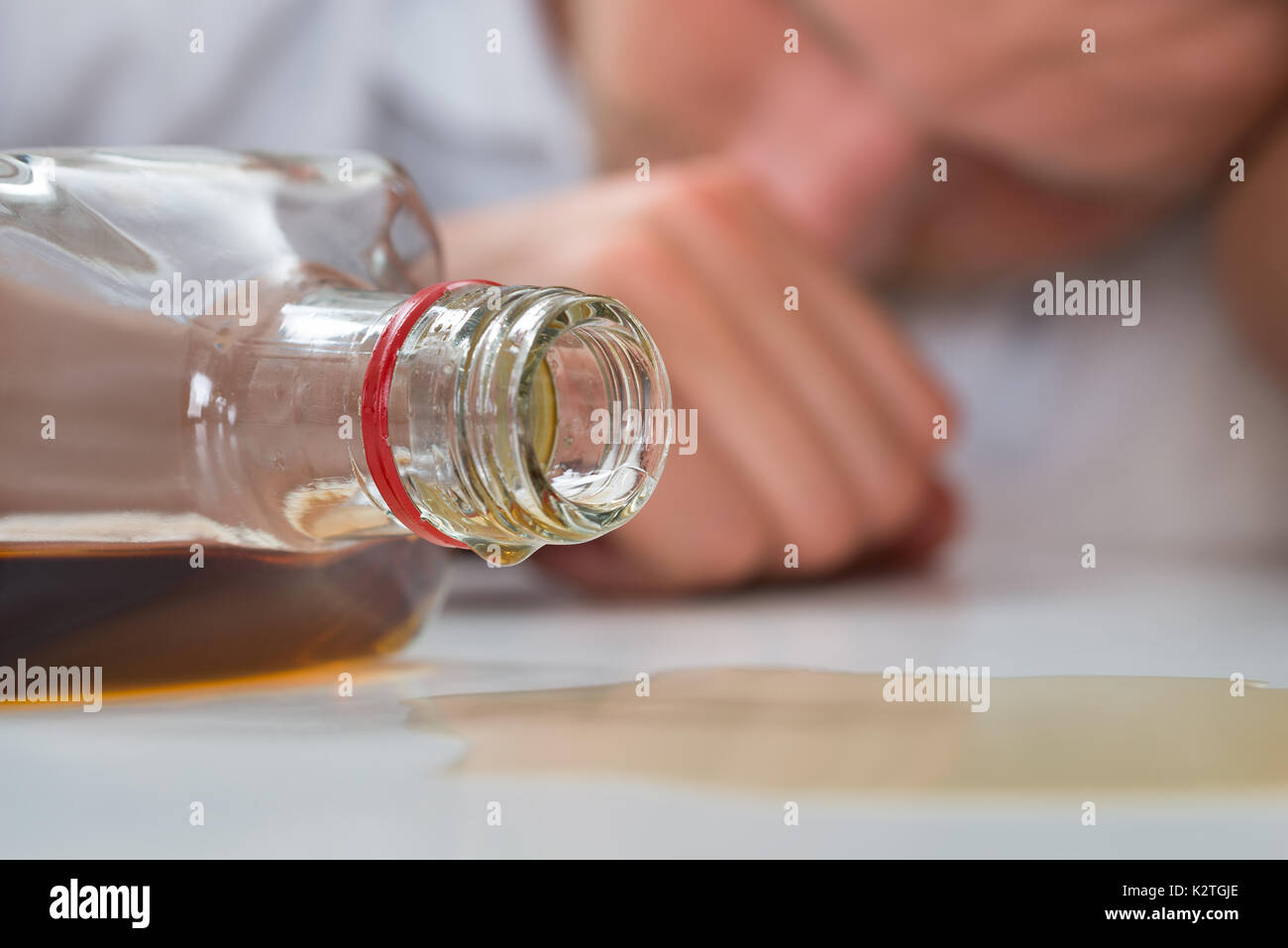 Giovane uomo ubriaco che dorme sul tavolo con una bottiglia di liquore Foto Stock