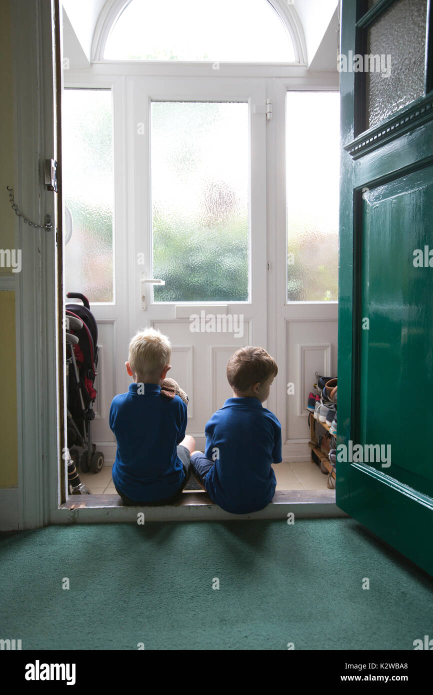 3 anni e 6 anno old boys seduti in una zona residenziale porta vestito in uniforme pronto a tornare a scuola, London, England, Regno Unito Foto Stock