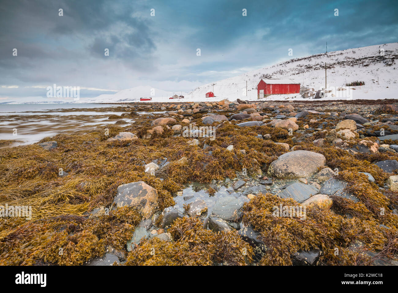 Tipici norvegesi calda e accogliente casa situata sulla riva del lago a un fiordo nel Troms County, Norvegia. Il sole basso sopra l'orizzonte e il cielo si è oscurato Foto Stock