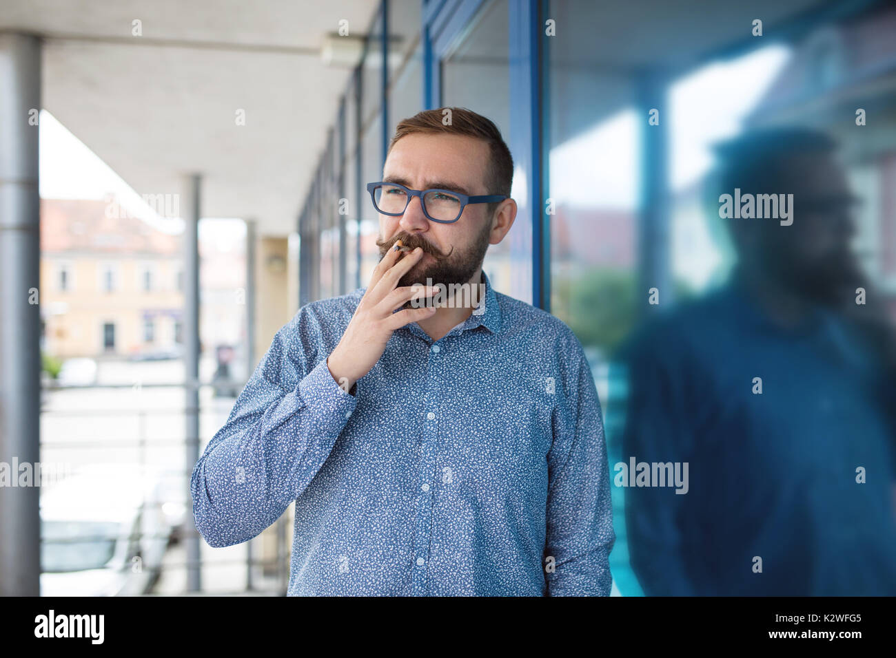 Uomo in camicia blu in piedi al di fuori dell'ufficio e il fumo di sigaretta Foto Stock