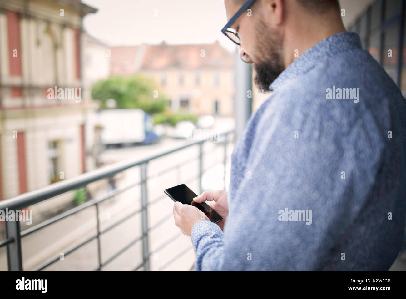 Uomo che utilizza smart phone e permanente al terrazzo. Foto Stock
