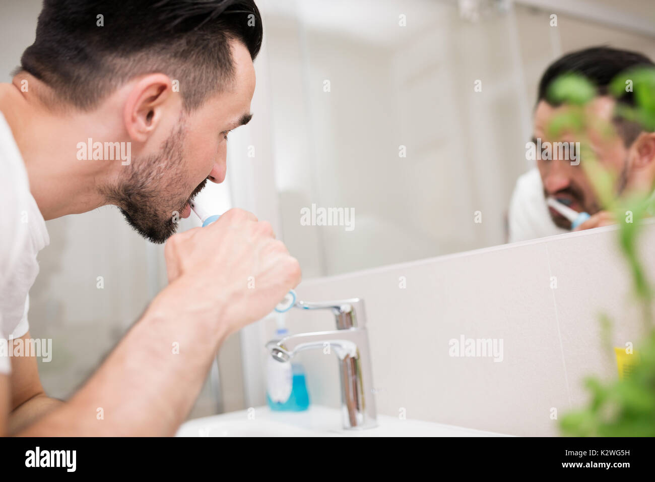 Attraente uomo spazzolatura dei denti nella sua stanza da bagno e guardando se stesso a specchio. Foto Stock