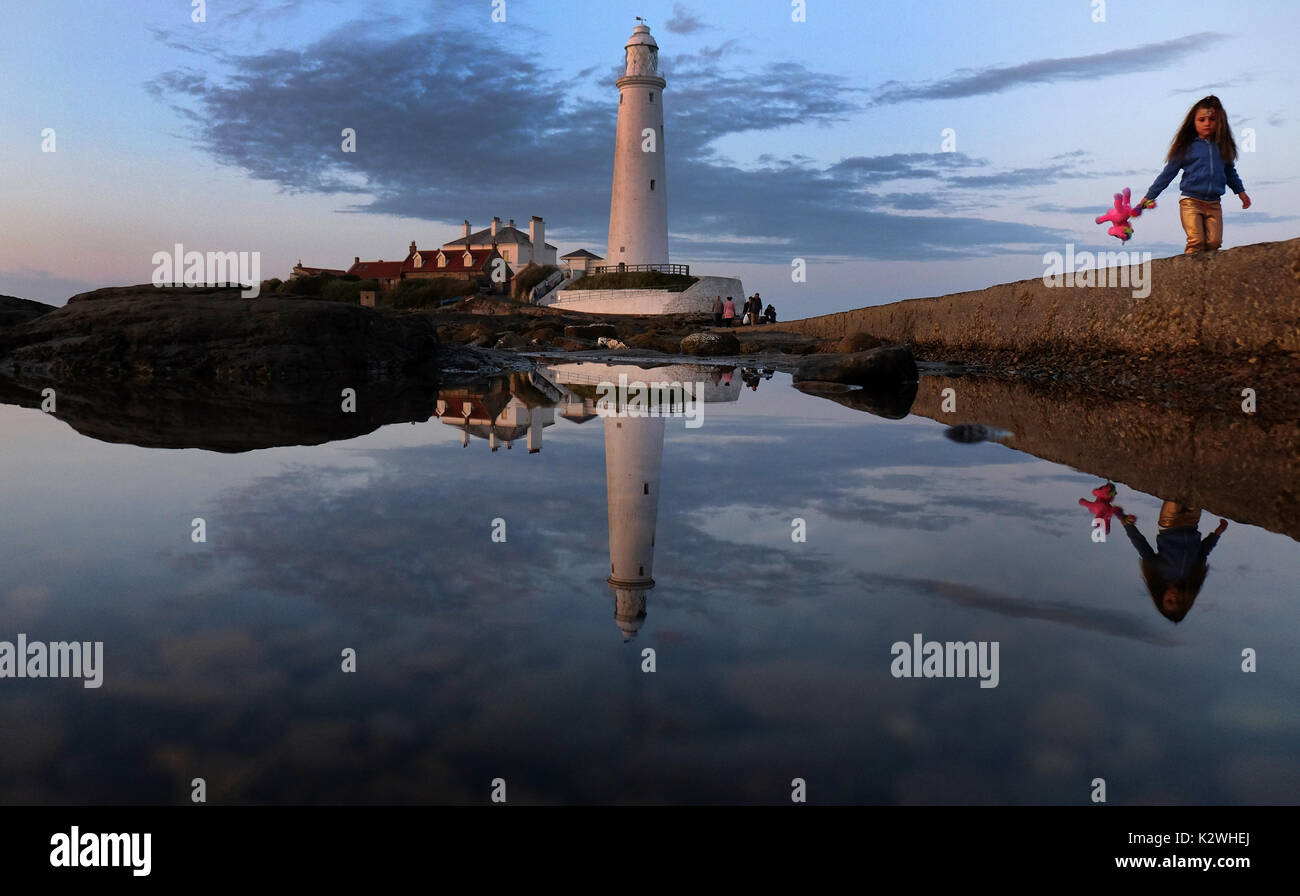 Una ragazza (nome non dato ma il permesso dei genitori dato) passeggiate passato St Mary's Lightouse come essa viene riflessa a Whitley Bay, North Tyneside, l'ultimo giorno di estate meteorologica. Foto Stock