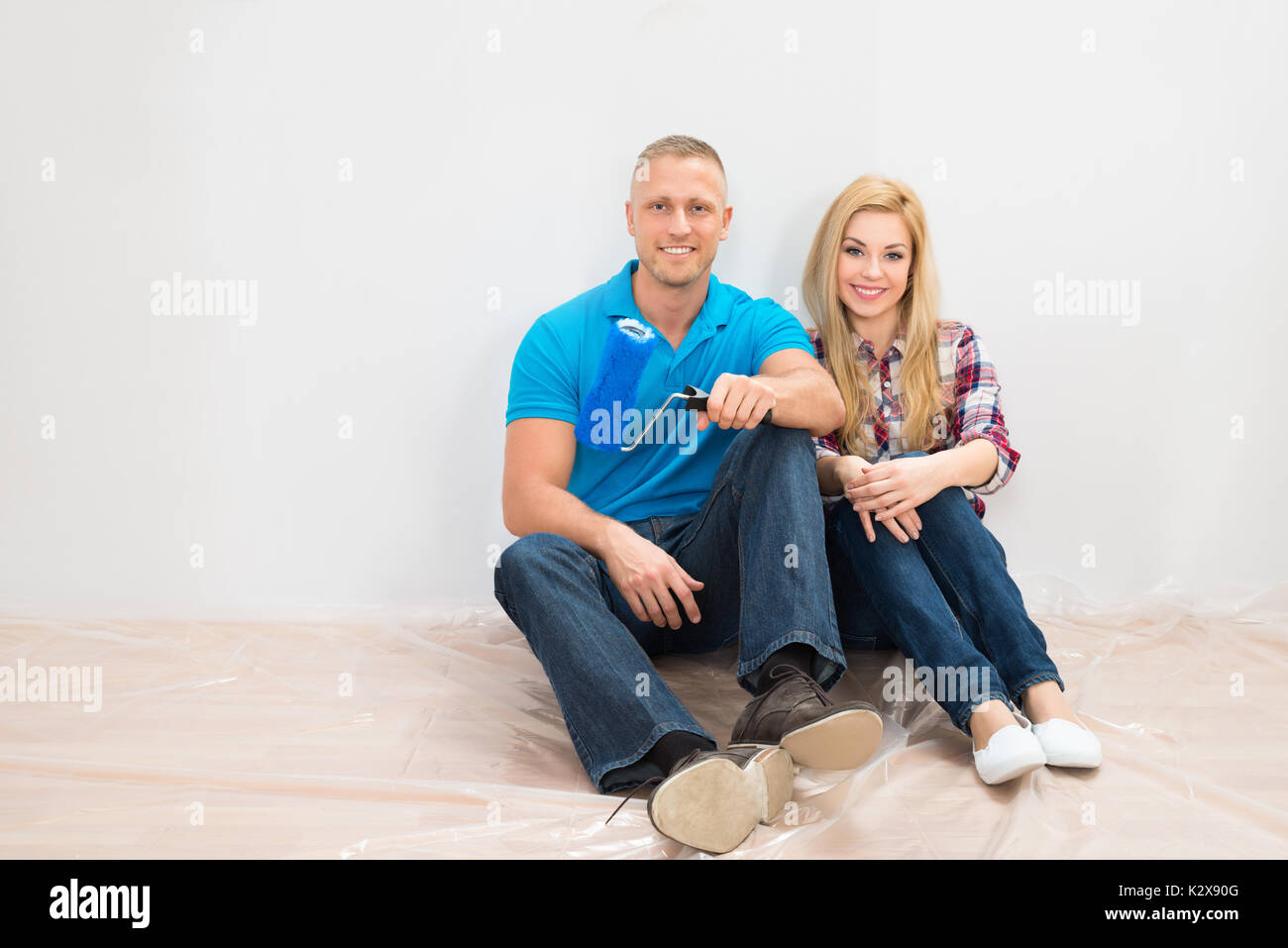 Giovane seduto sul pavimento a sorridere di fronte parzialmente parete dipinta in Home Foto Stock