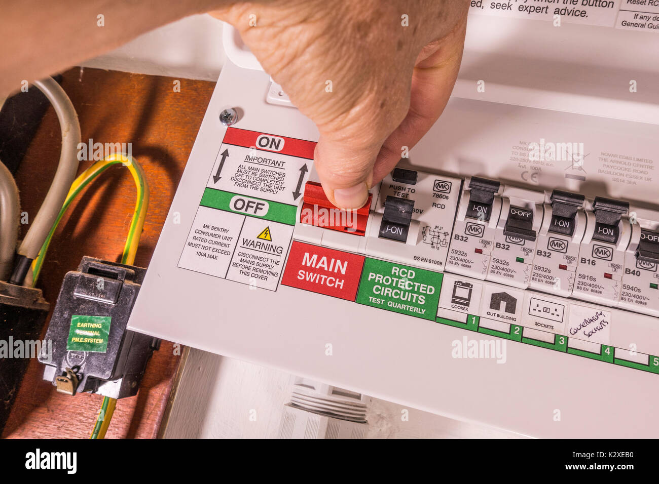 L uomo del dito e il pollice sull'l'interruttore principale on/off di uno appena montato consumatore di elettricità unità, con più switch. Inghilterra, Regno Unito. Foto Stock