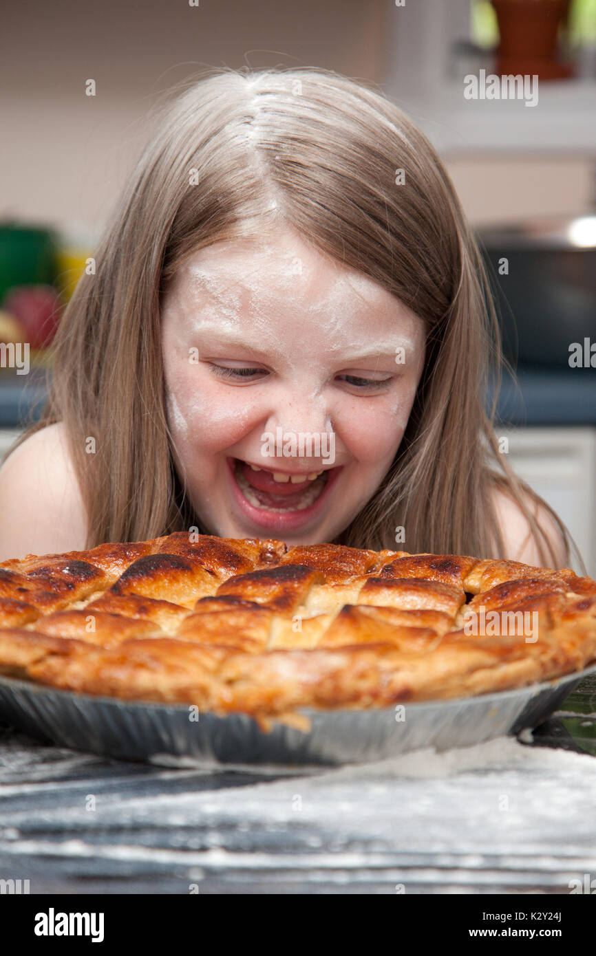 Una bambina ricoperti di farina dopo la cottura o cibo lotta ridendo e guardando sopra una fetta di torta di mele. Foto Stock