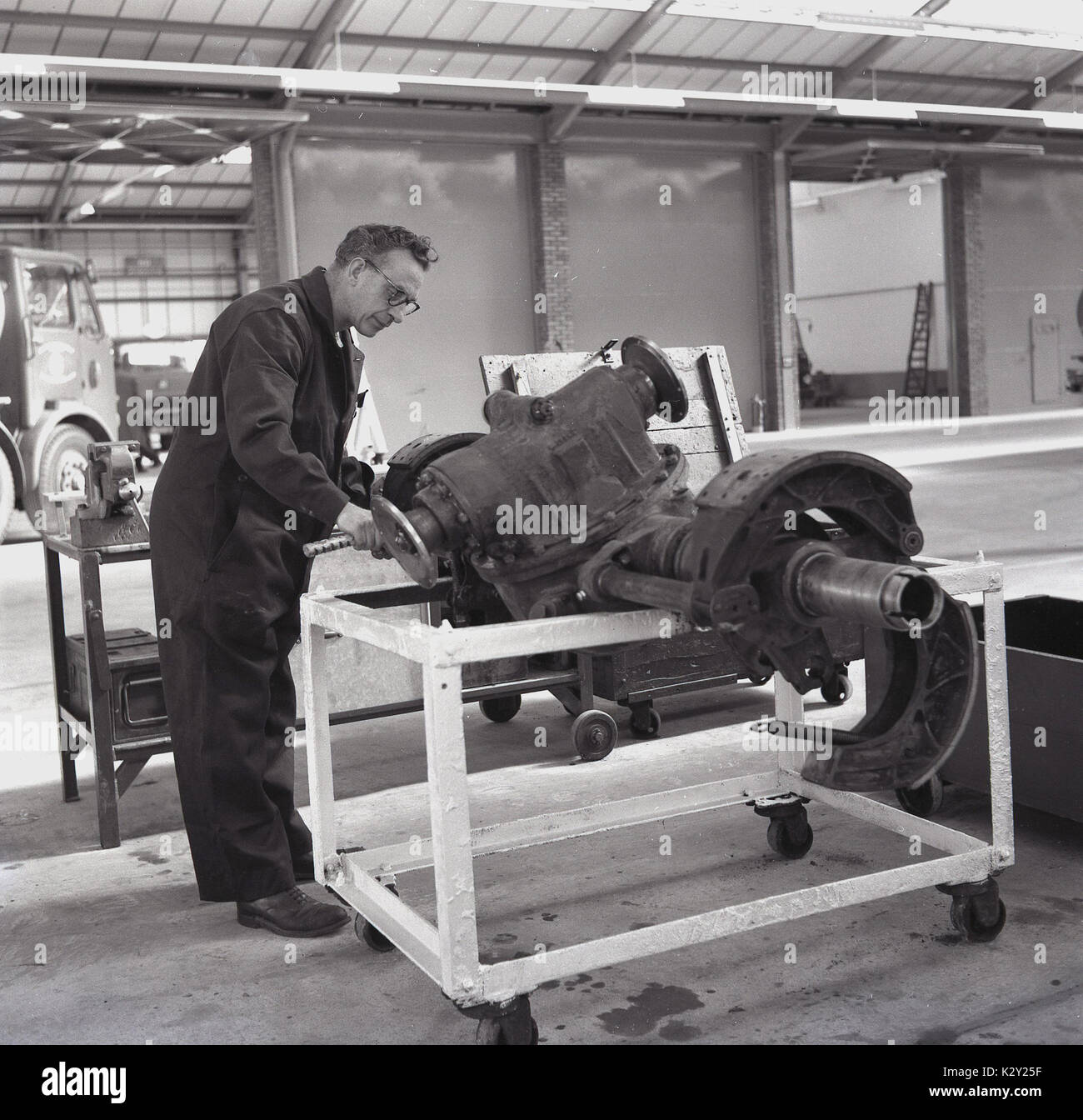Anni sessanta, storico, maschio motore controllo meccanico di una grande pesante carrello anteriore assale e le parti associate all'interno di un workshop, Inghilterra, Regno Unito. Foto Stock