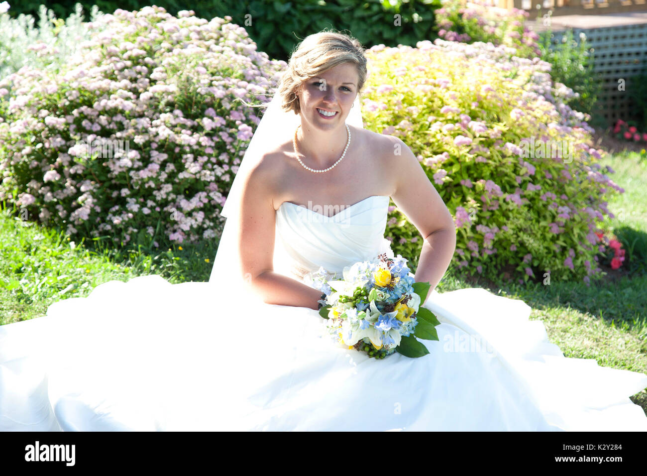 Una sposa in un bel bianco principessa abito si siede in un giardino soleggiato Foto Stock