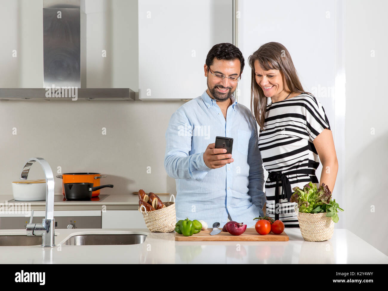 Giovane guardando il messaggio ricevuto in corrispondenza di un telefono cellulare durante la preparazione di cibo in una cucina Foto Stock