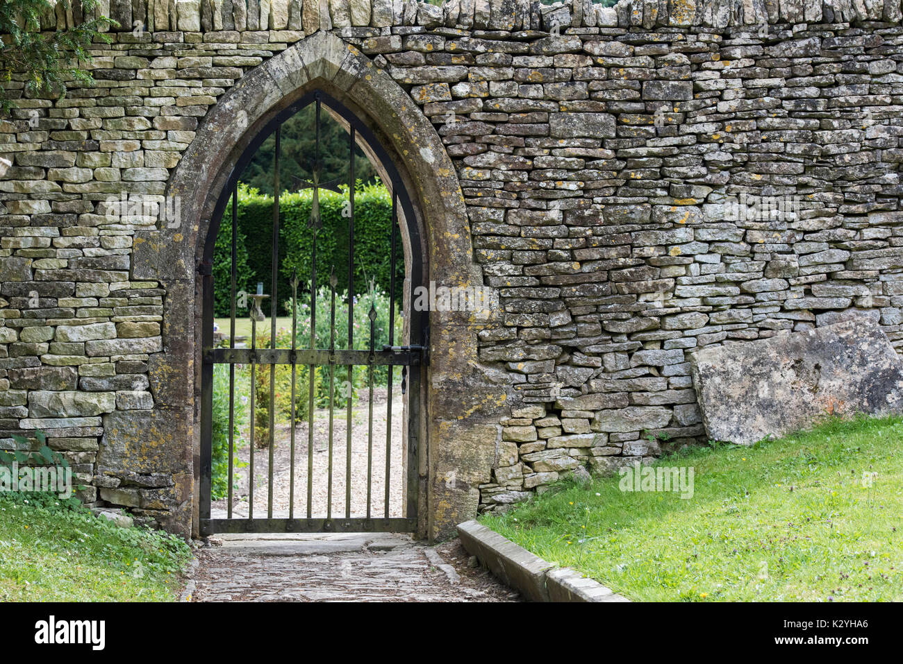 Gated arcuato portale ed una parete di pietra entro i motivi di St Andrew's sagrato, Chedworth, Cotswolds, Gloucestershire, Inghilterra Foto Stock
